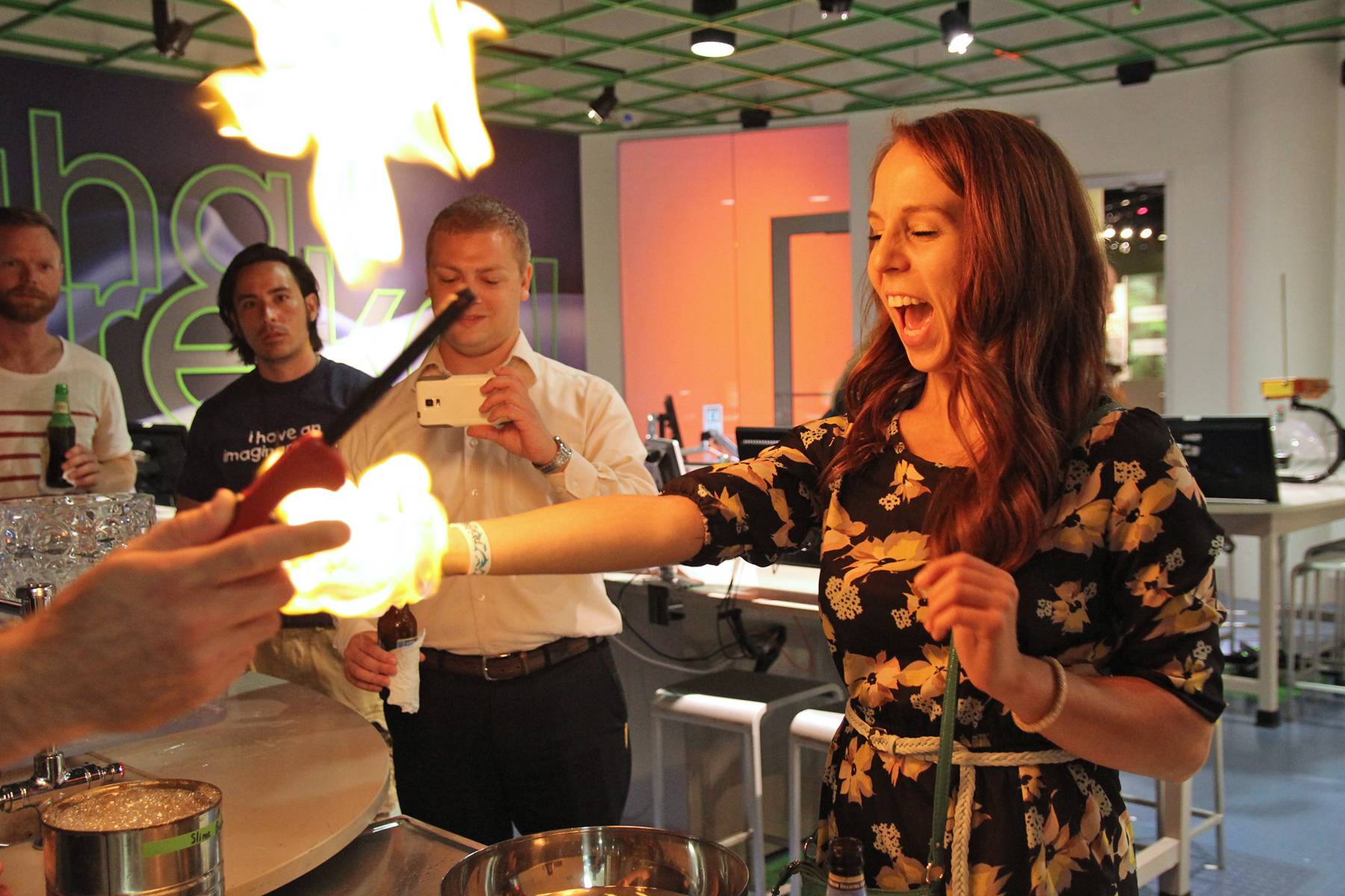 A guest reacting to a fire experiment while others enjoy drinks at a past Science on the Rocks night